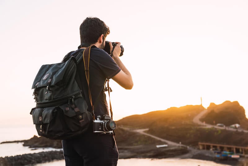 日落时分，带着古董相机和旅行背包的男人